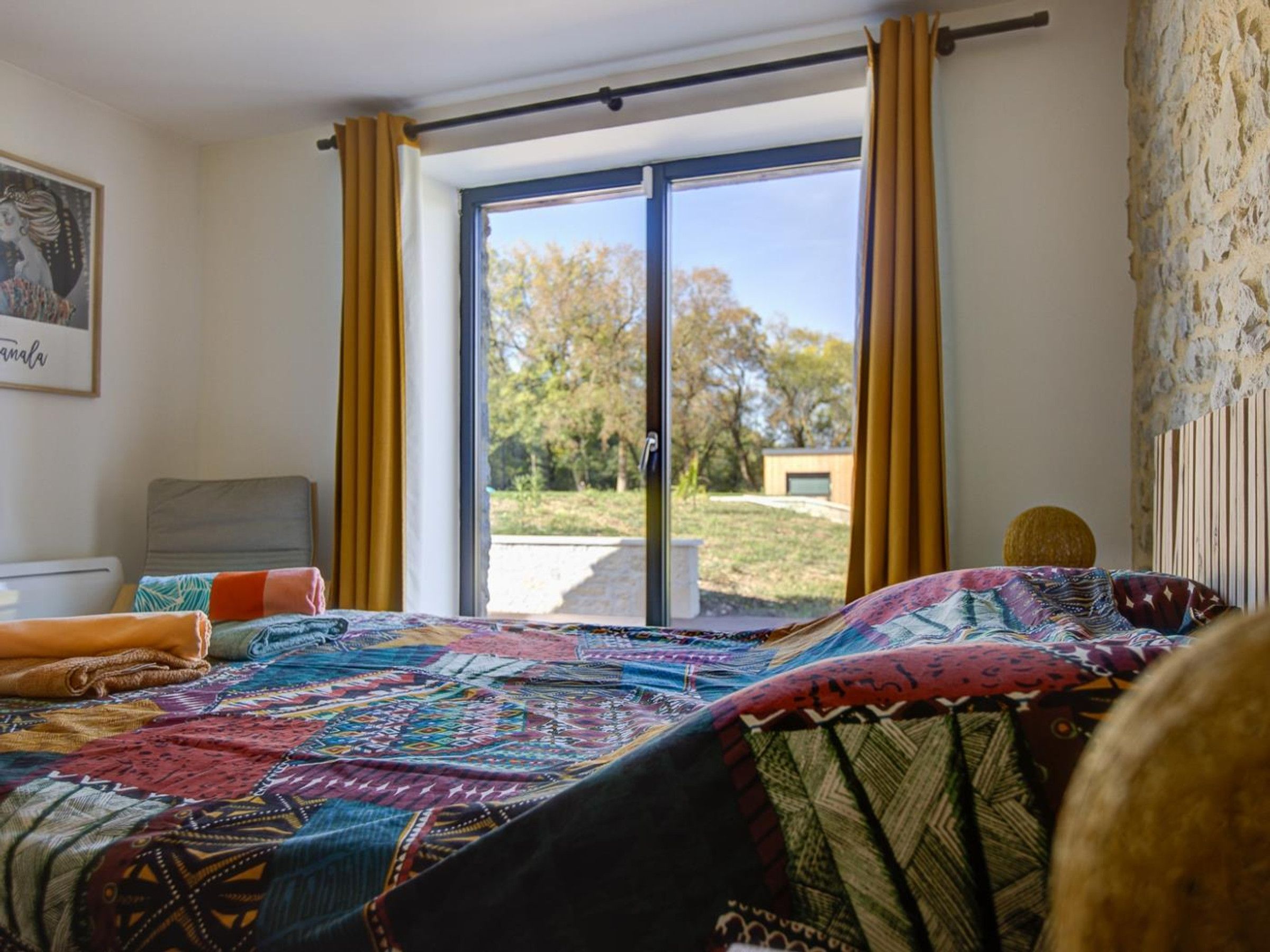 A bedroom with a large bed, a window with curtains, a view of the outdoors, and a painting on the wall.