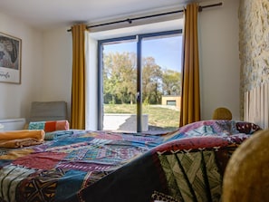 A bedroom with a large bed, a window with curtains, a view of the outdoors, and a painting on the wall. - Restored house with private pool - 6 guests (Montfaucon)