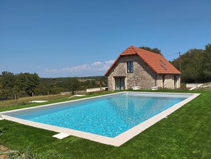 Ein Steinhaus mit rotem Dach und einem Schwimmbad davor.