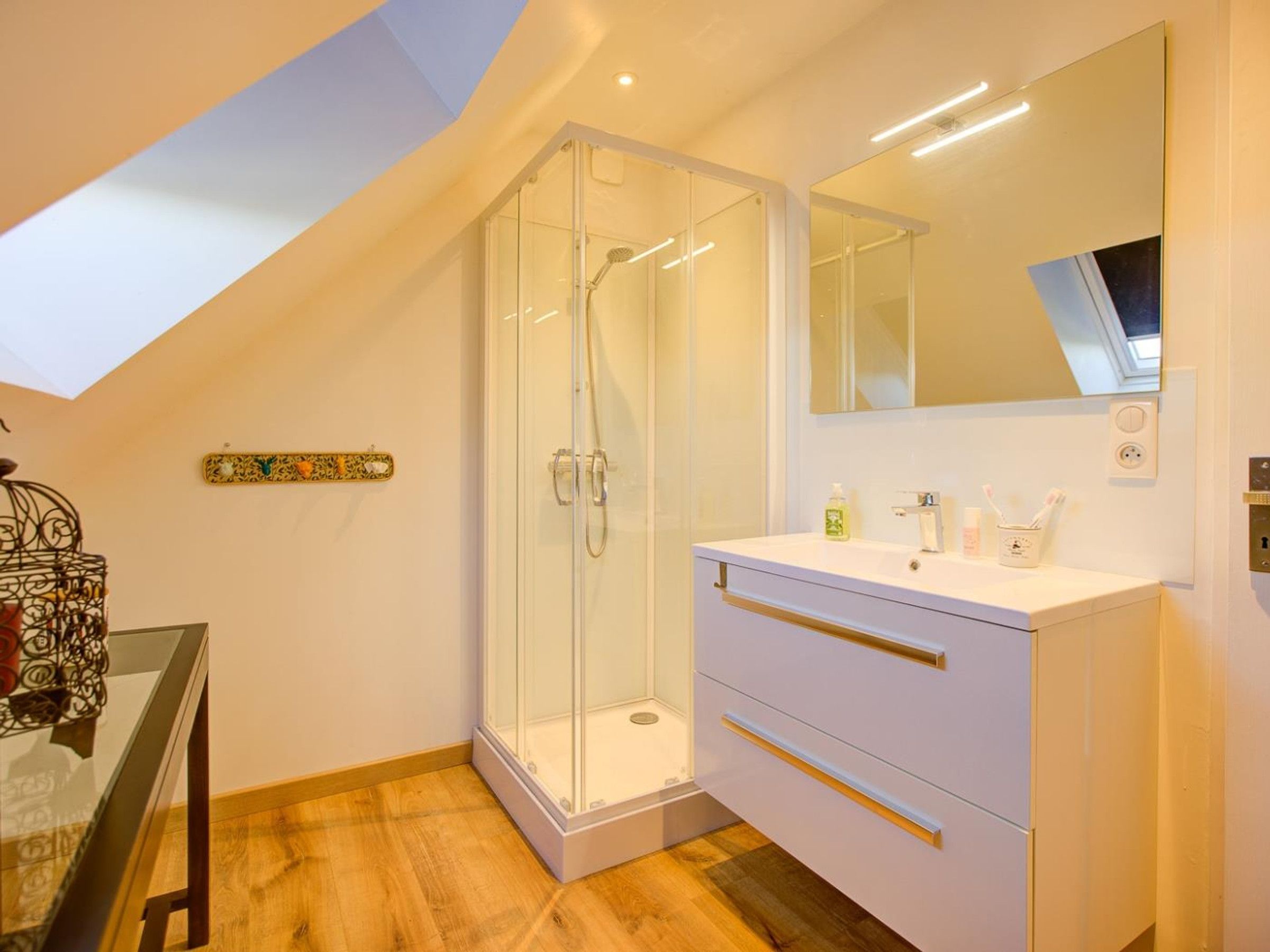 Une salle de bain moderne avec une douche à parois de verre, un meuble-lavabo blanc doté de tiroirs et un grand miroir.