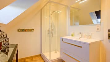 Un baño moderno con cabina de ducha acristalada, un tocador blanco con cajones y un espejo grande.