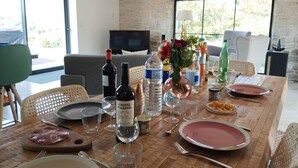 Uma mesa de jantar posta com pratos, talheres, garrafas de vinho, copos e um vaso com flores.