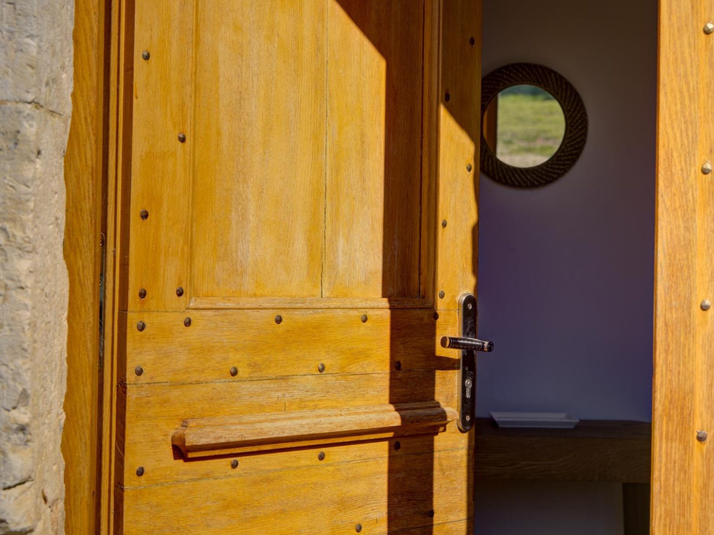 Een houten deur met een handgreep en een sleutelgat, die leidt naar een kamer met een ronde spiegel aan de muur.