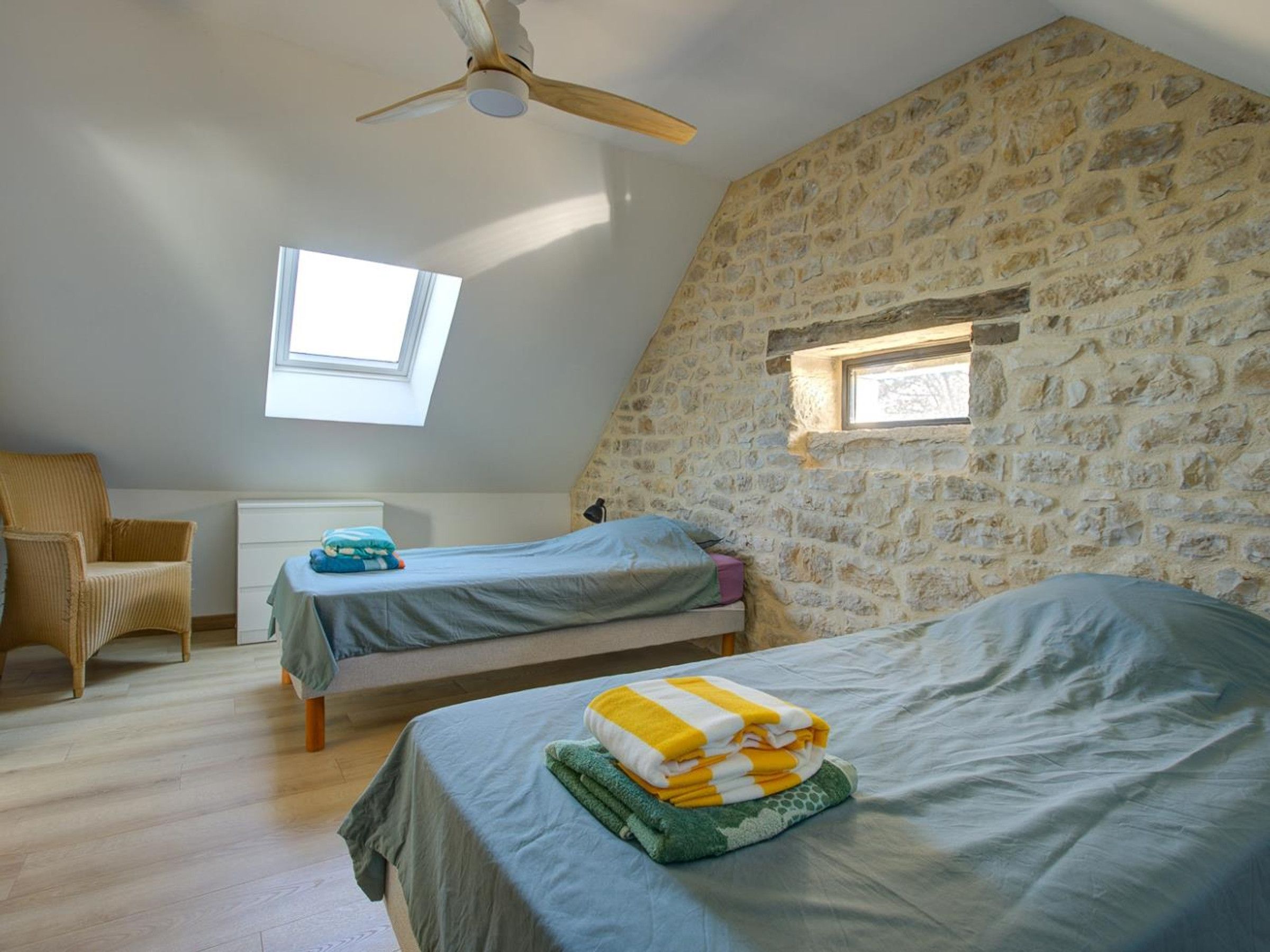 Ein Schlafzimmer mit zwei Betten, einem Deckenventilator und einer Steinwand.
