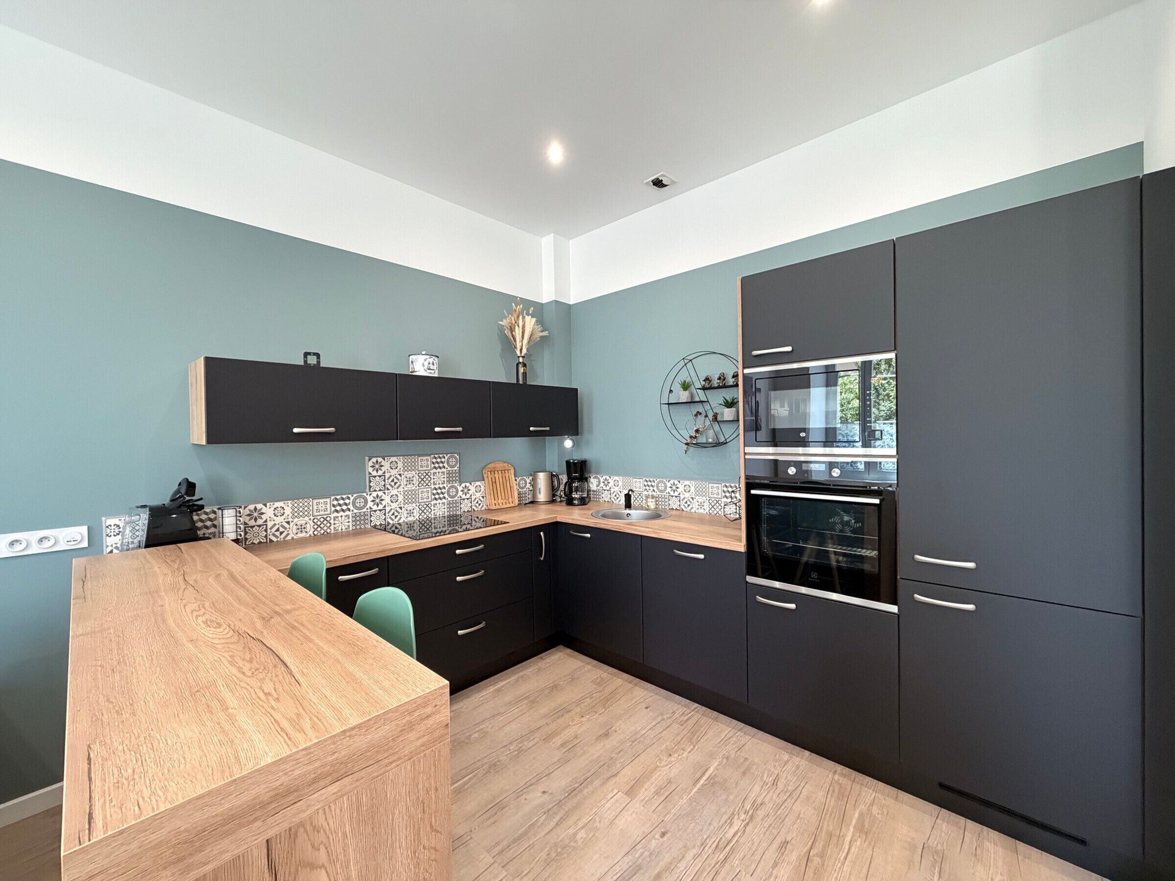 Une cuisine moderne avec des meubles de couleur sombre, un plan de travail en bois et un revêtement mural en carreaux.