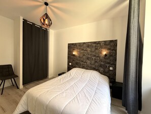 A bedroom with a bed, a chair, a nightstand, a wall-mounted light fixture, and a curtain. - Apartment in city center with WIFI - 6 guests (La Bourboule)