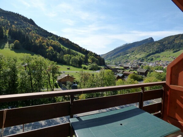 A balcony with a view of a valley, a town, and mountains.