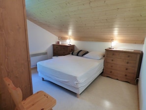 Une chambre à coucher avec un lit simple, deux tables de chevet, une commode en bois et une chaise.