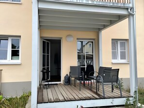 Katettu ulkotila, jossa on pöytä ja tuoleja, patsas sekä ovi, joka johtaa sisätiloihin.
