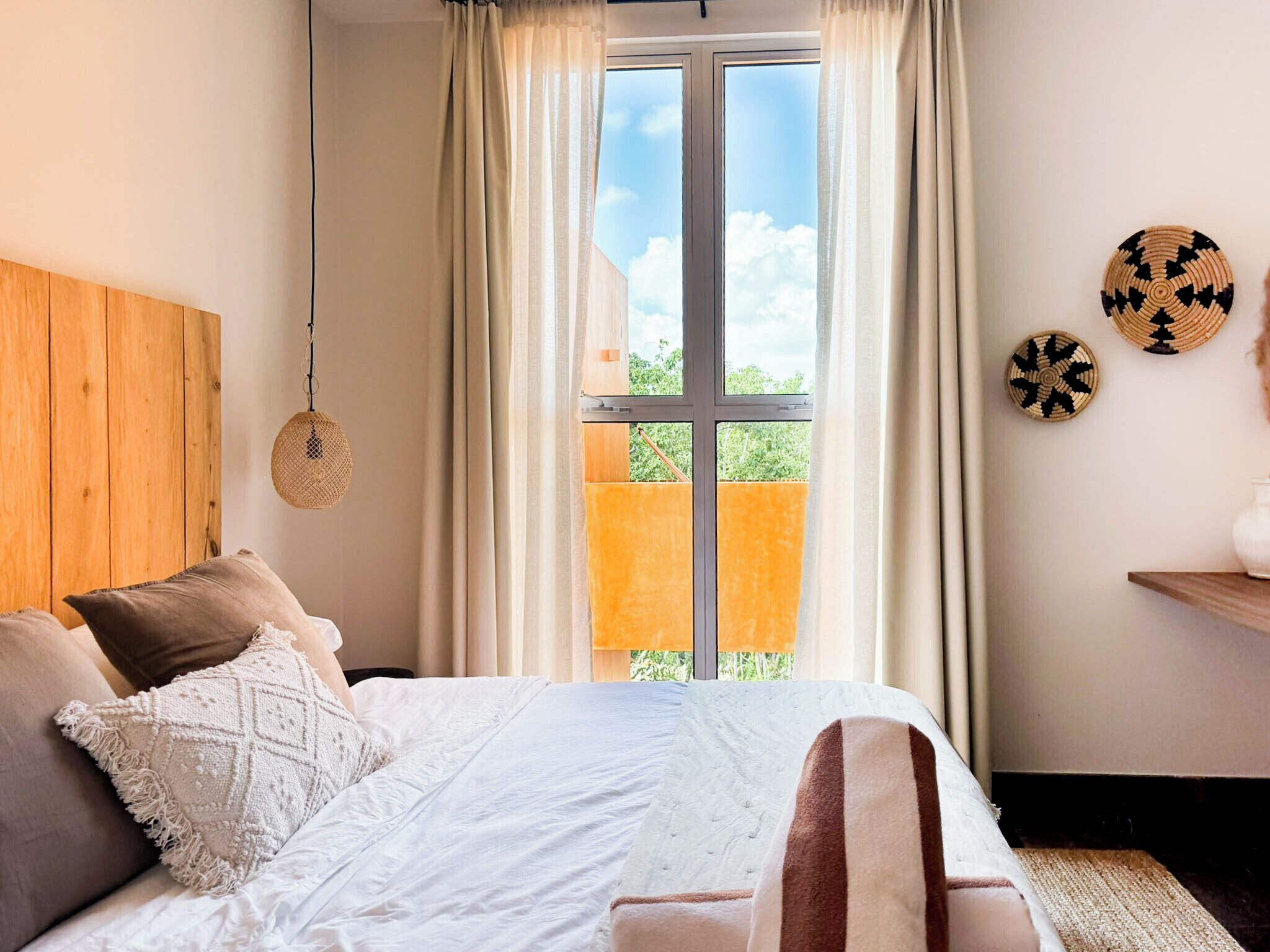 Une chambre avec une grande fenêtre, un lit avec une literie blanche et une vue sur un bâtiment à l’extérieur.