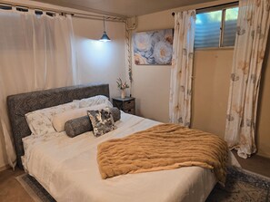 A bedroom with a large bed, a bedside table, a wall-mounted TV, and a window with curtains.