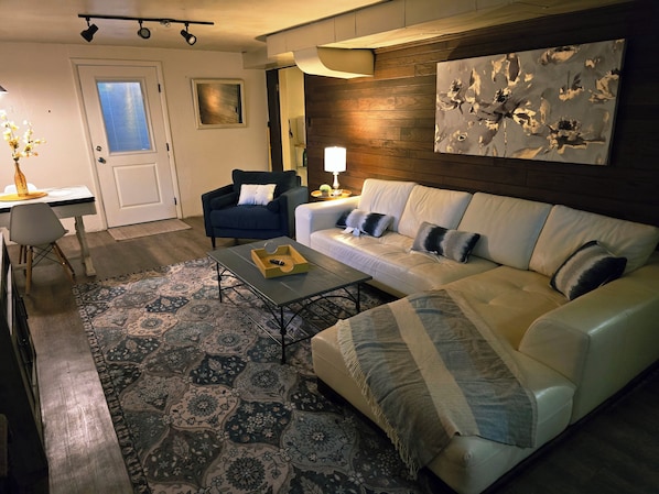 A living room with a sofa, armchairs, a coffee table, a rug, a painting, and a door with a window.
