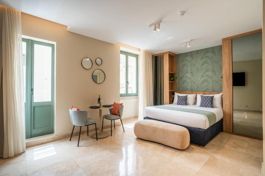 Un dormitorio moderno con cama, escritorio y silla. Hay una ventana con cortinas, un espejo montado en la pared y un televisor.