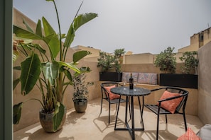En terrasse med et rundt bord og stole, omgivet af plantekasser og udsigt til bygninger.