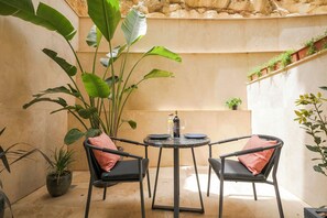 A small outdoor seating area with two chairs and a table, surrounded by large green plants. - The Three Doors (St. Julian's)