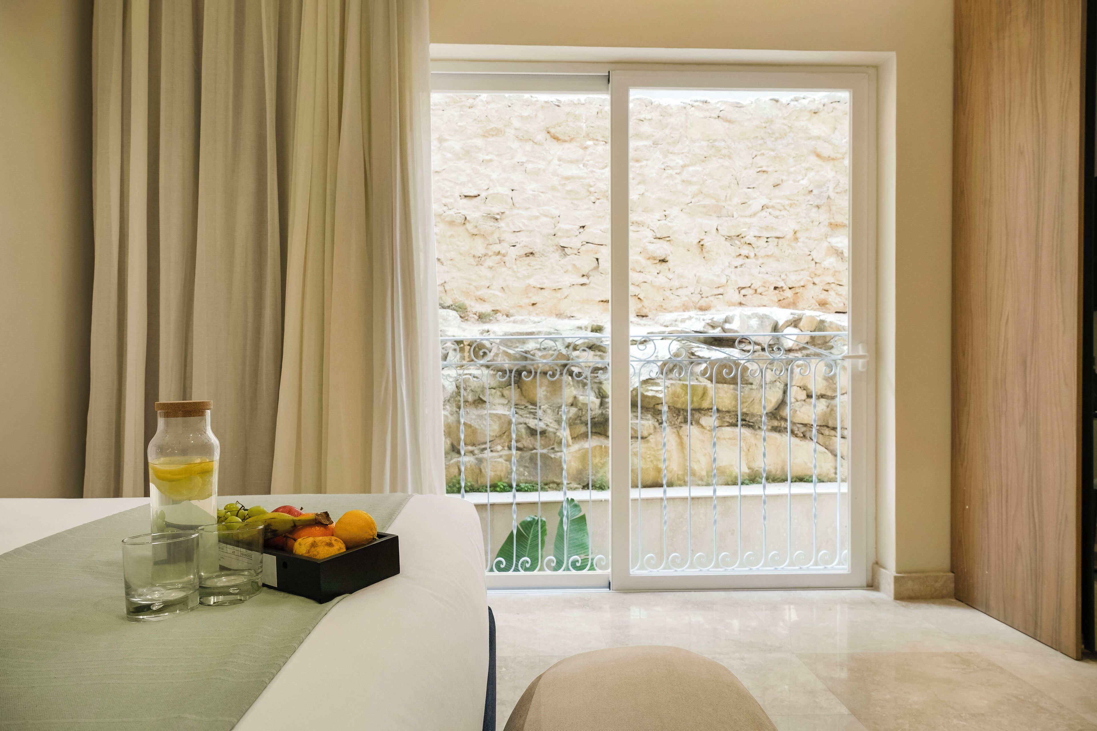 Una camera d'albergo con un letto, un tavolo con una ciotola di frutta, una bottiglia e dei bicchieri.