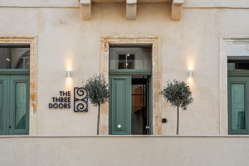 Facciata di un edificio con un'insegna che recita 'THE THREE DOORS' e due applique illuminate.