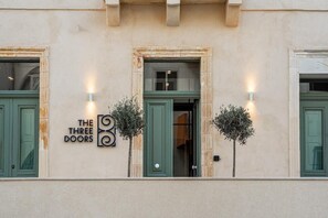 A building facade with a sign reading 'THE THREE DOORS' and two lit wall sconces. - The Three Doors (St. Julian's)