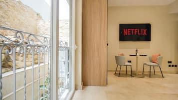 Un interior moderno con una gran pantalla de televisión mostrando 'NETFLIX', un comedor con dos sillas y un balcón con barandillas de metal.