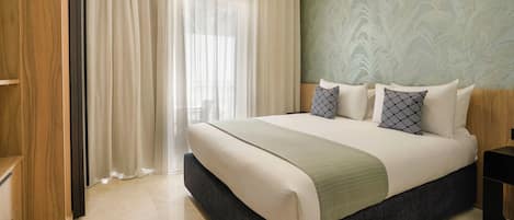 Habitación de hotel con una cama grande, un armario de madera y vistas al exterior a través de cortinas translúcidas.