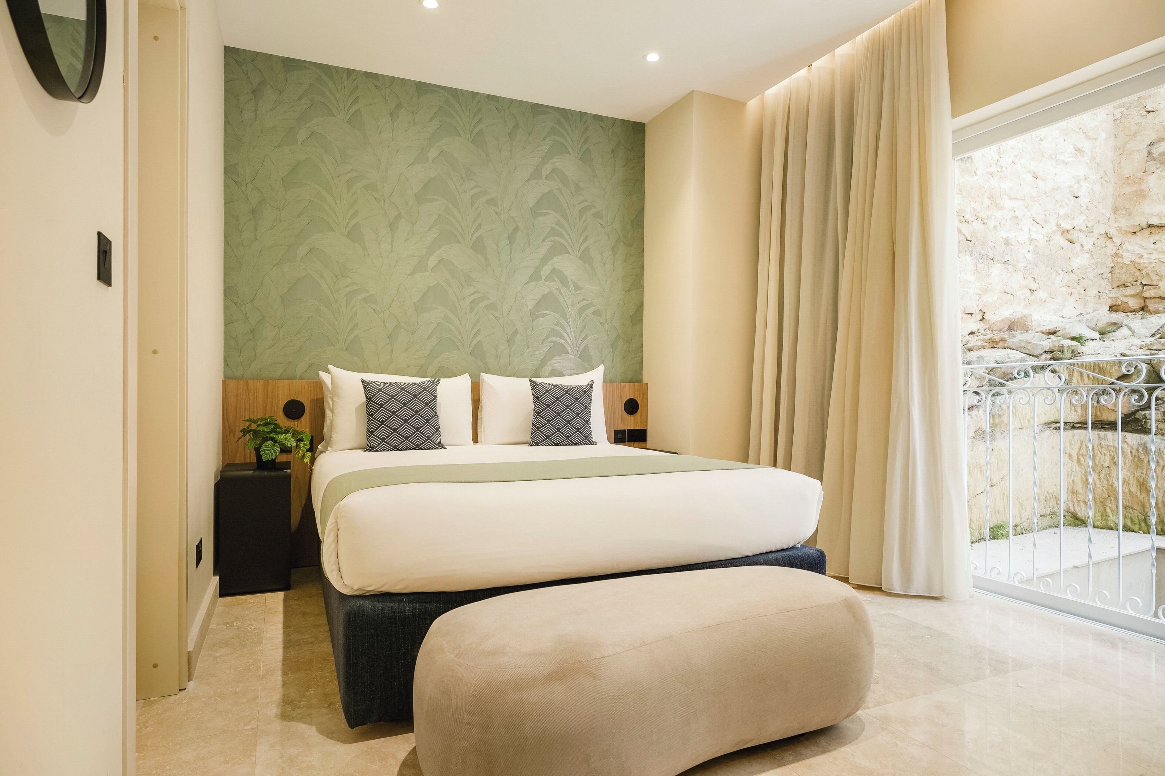 A bedroom with a bed, a nightstand, a potted plant, and a view of a balcony.