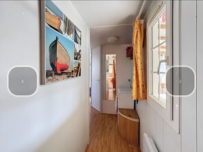 Ein schmaler Flur mit Holzboden, einer weißen Tür und einem an der Wand hängenden Bild.