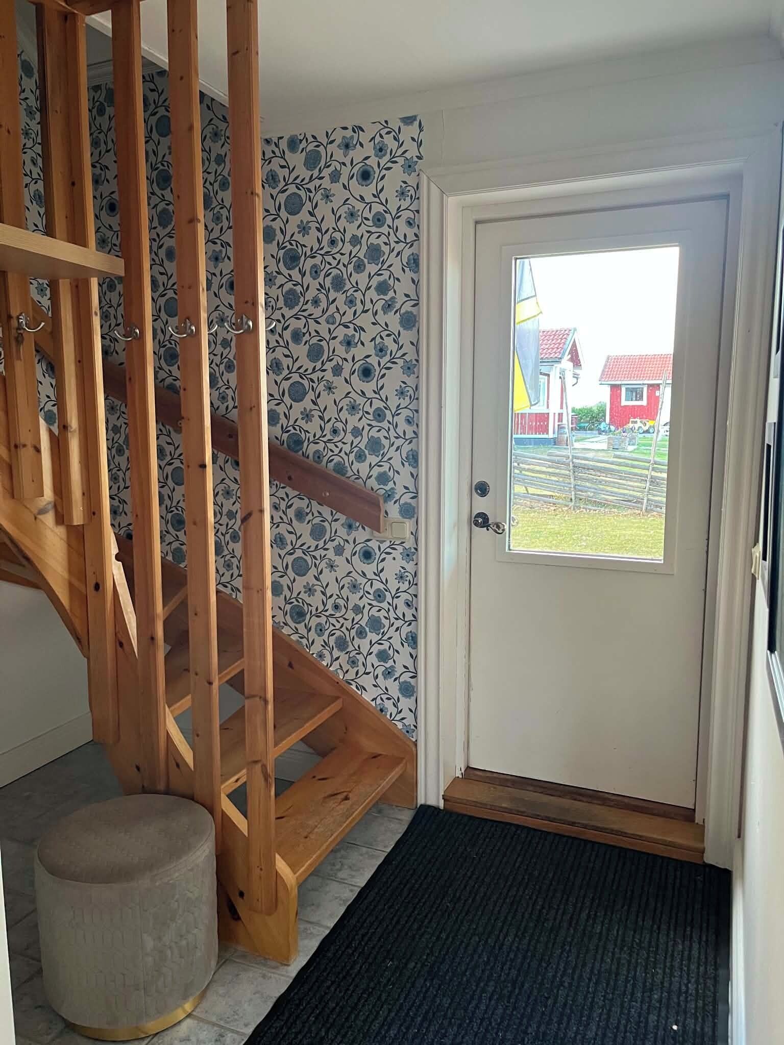 A wooden staircase leading to a landing with a patterned wall and a door with a view of a red house outside.
