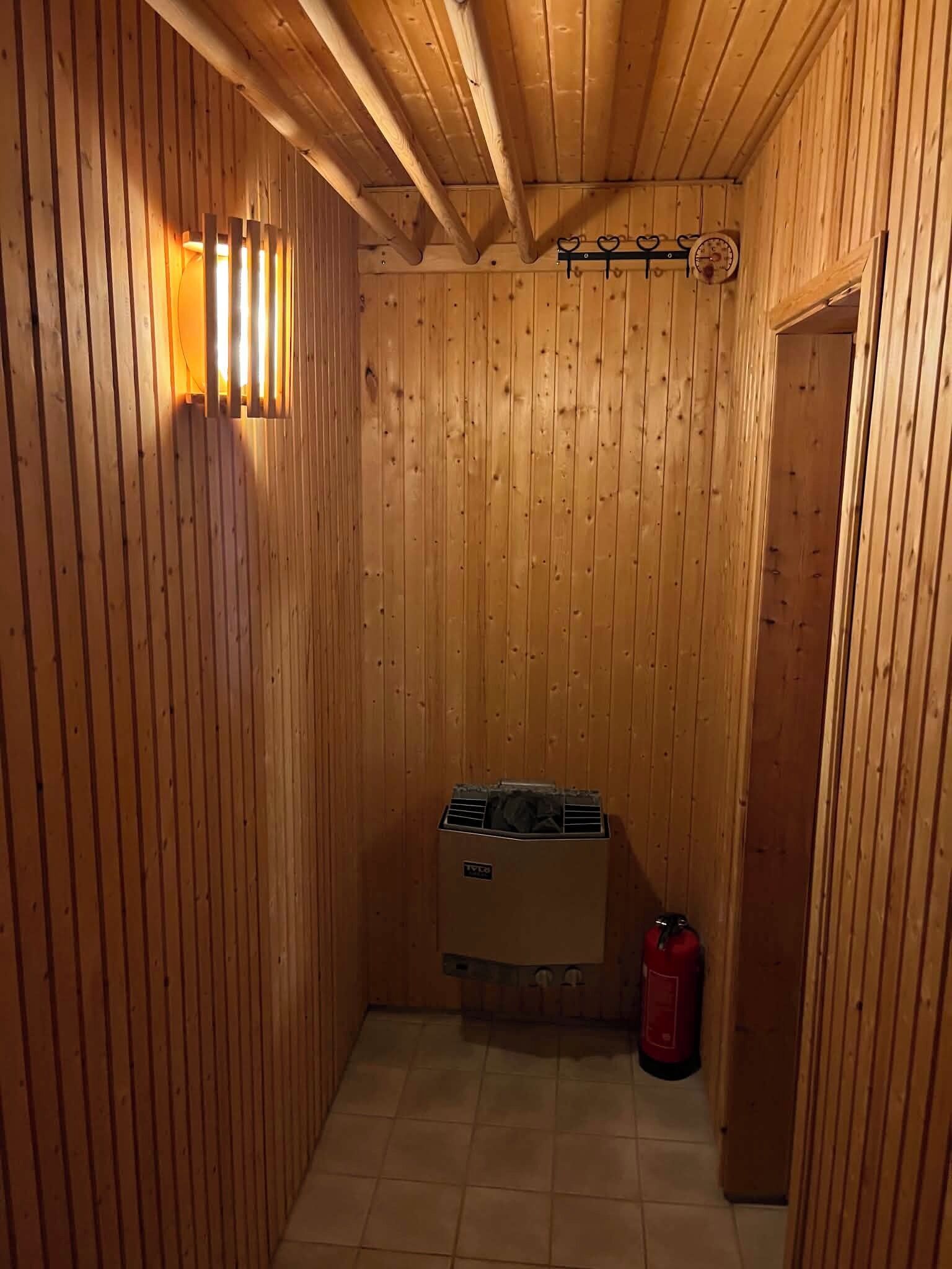 A wooden sauna room with a bench, a towel rack, and a fire extinguisher.