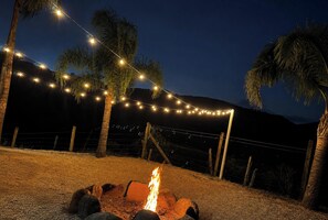 A nighttime outdoor setting with a fire pit, string lights, and palm trees. - Celeiro Taquaras em Rancho Queimado - SC (Taquaras)