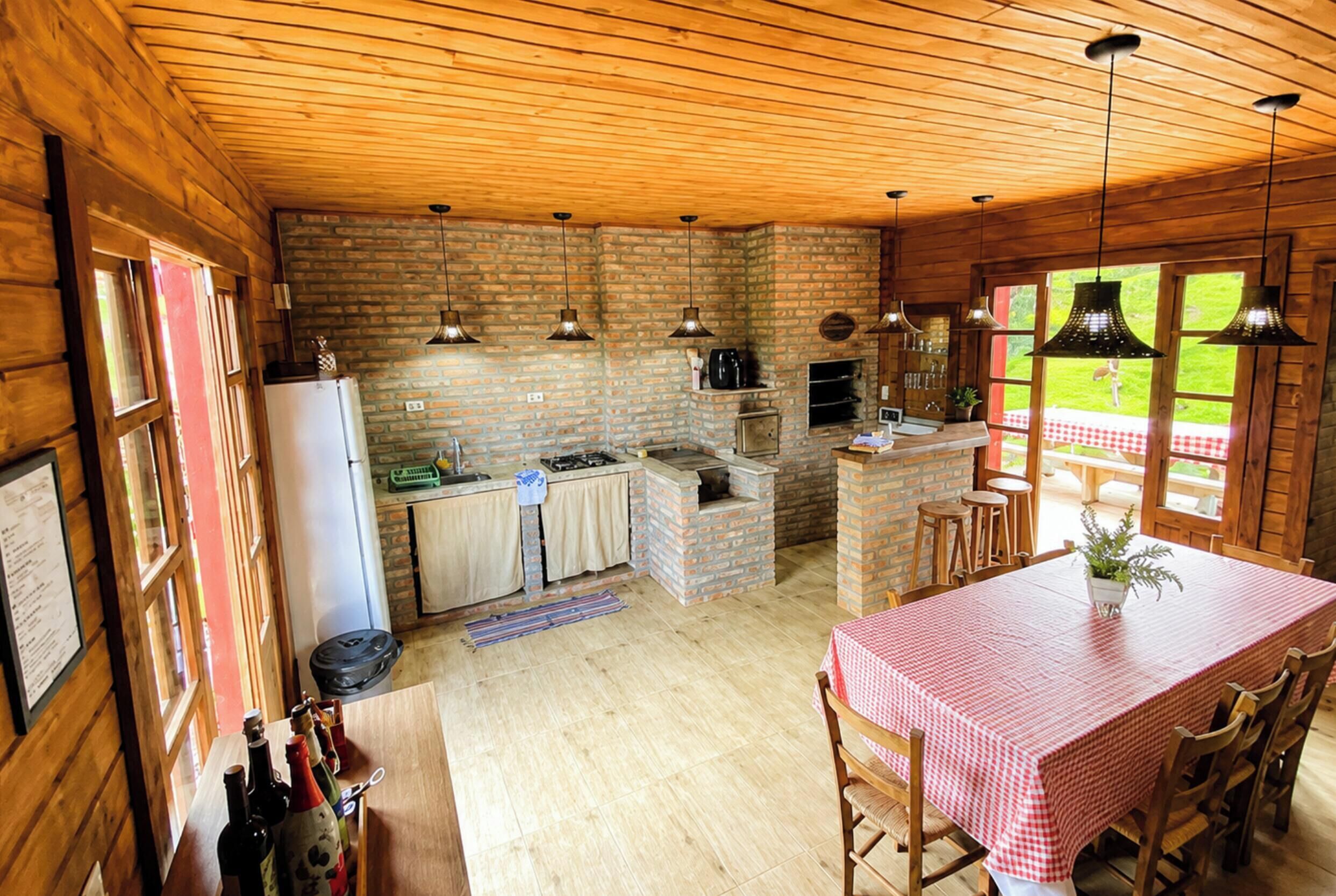 Een landelijke keuken met een bakstenen muur, houten plafond en een eethoek met geruit tafelkleed.