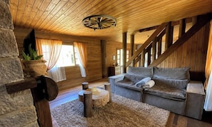 A cozy cabin interior with a wooden ceiling, a sofa, a small round table, and a potted plant.