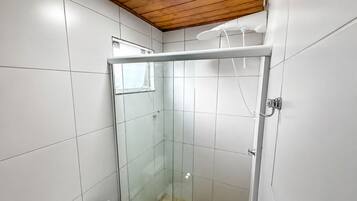 Pequeño espacio de ducha cerrado con puerta de cristal, paredes de azulejos blancos y techo de madera.