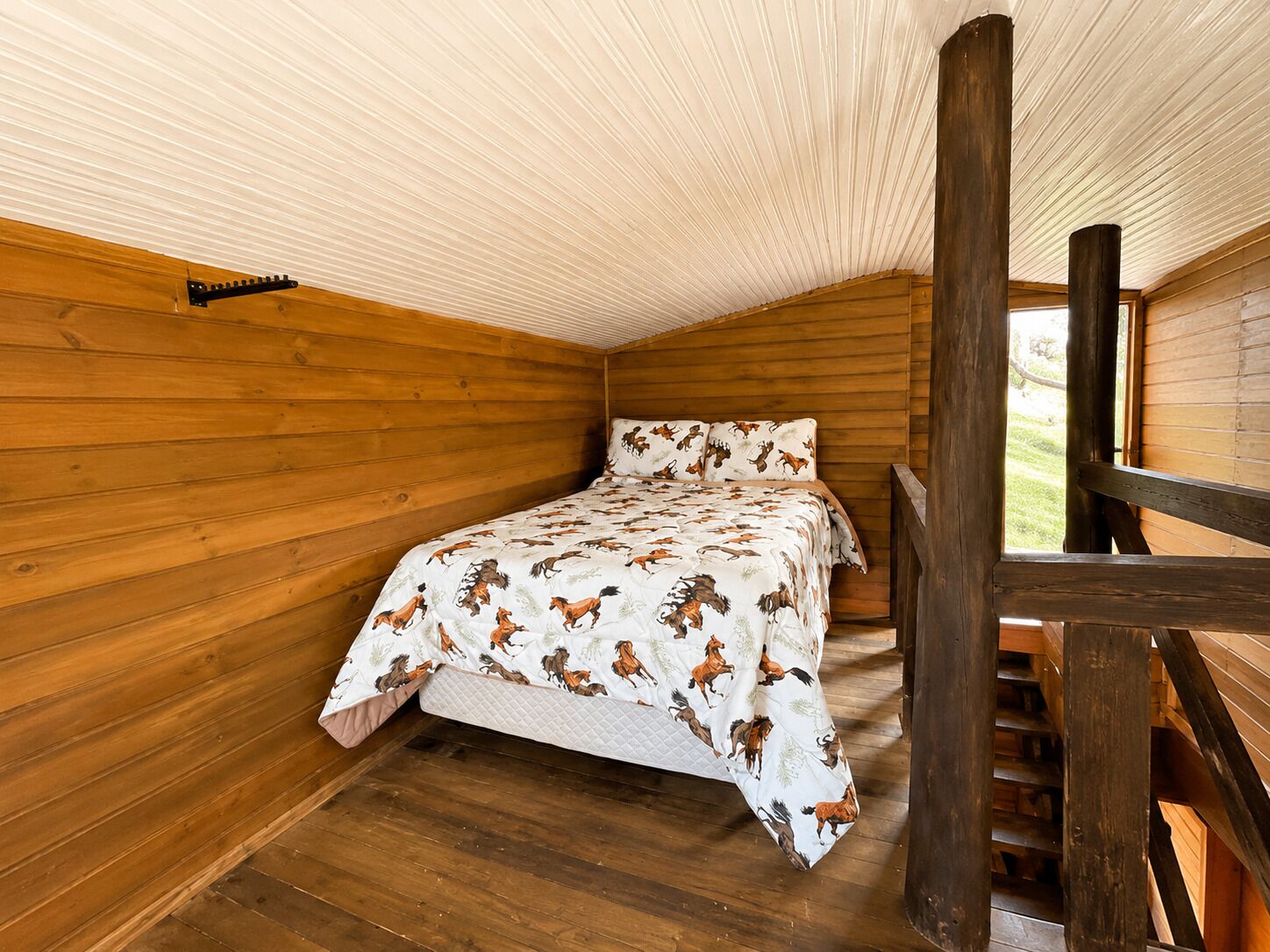 Une chambre à coucher avec un lit, des murs en bois, une fenêtre et un escalier en bois.