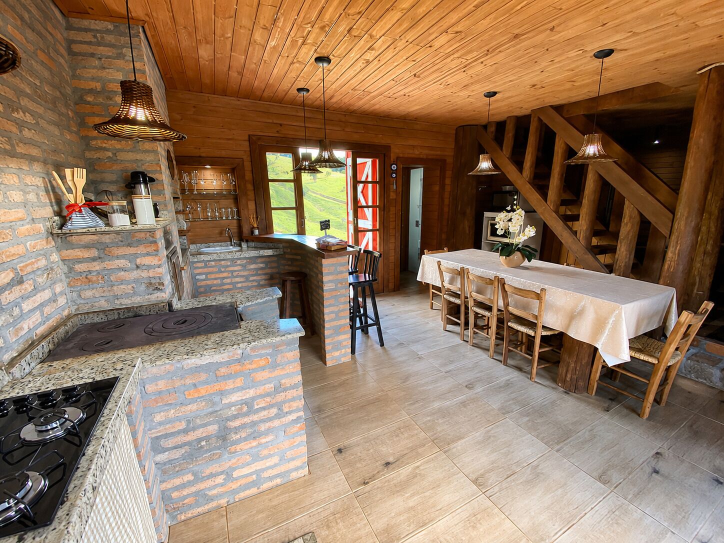 A rustic kitchen with a brick stove, wooden ceiling, and a dining area with a table and chairs.