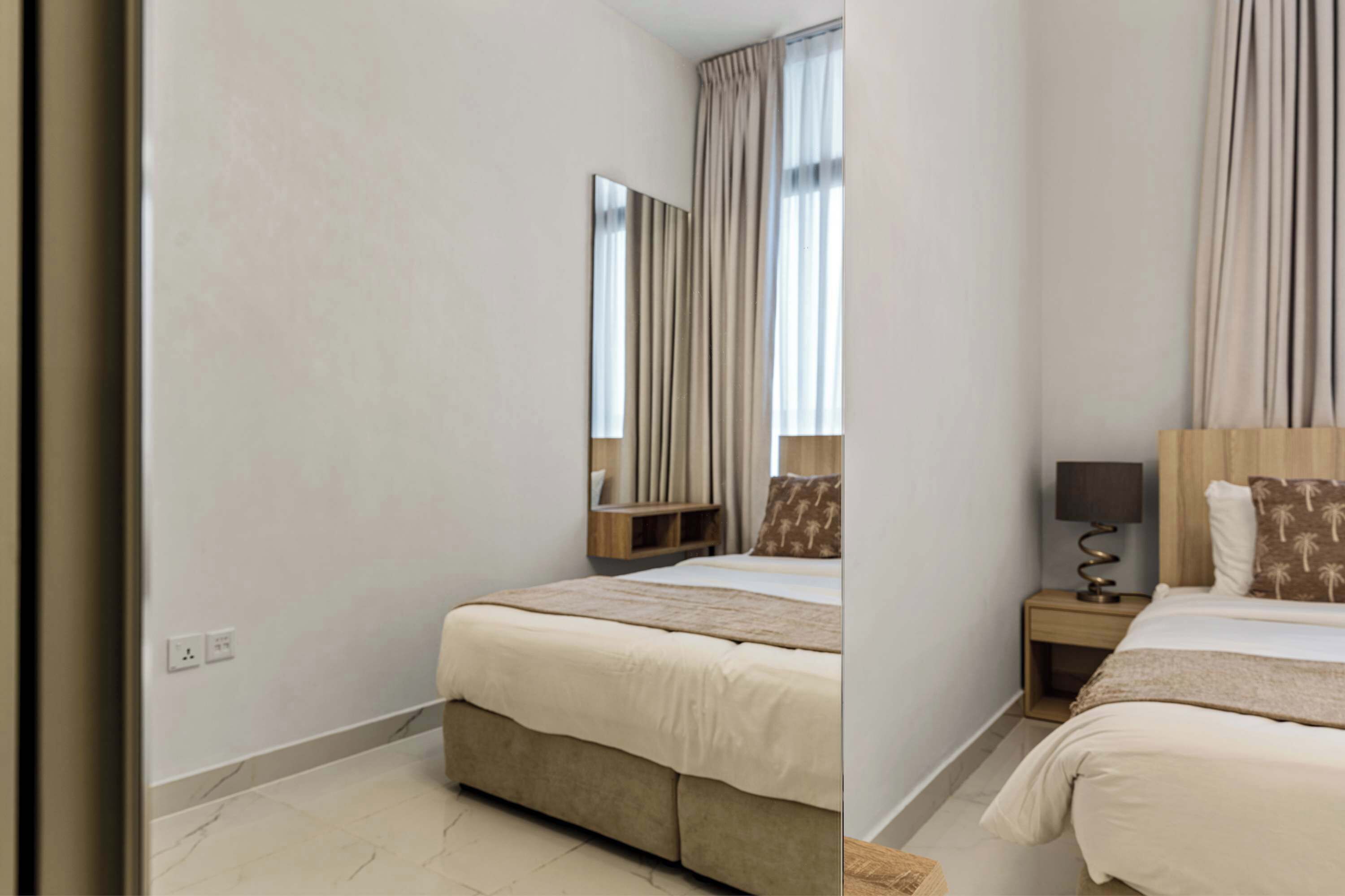 A hotel room with a bed, bedside table, lamp, and a mirror.
