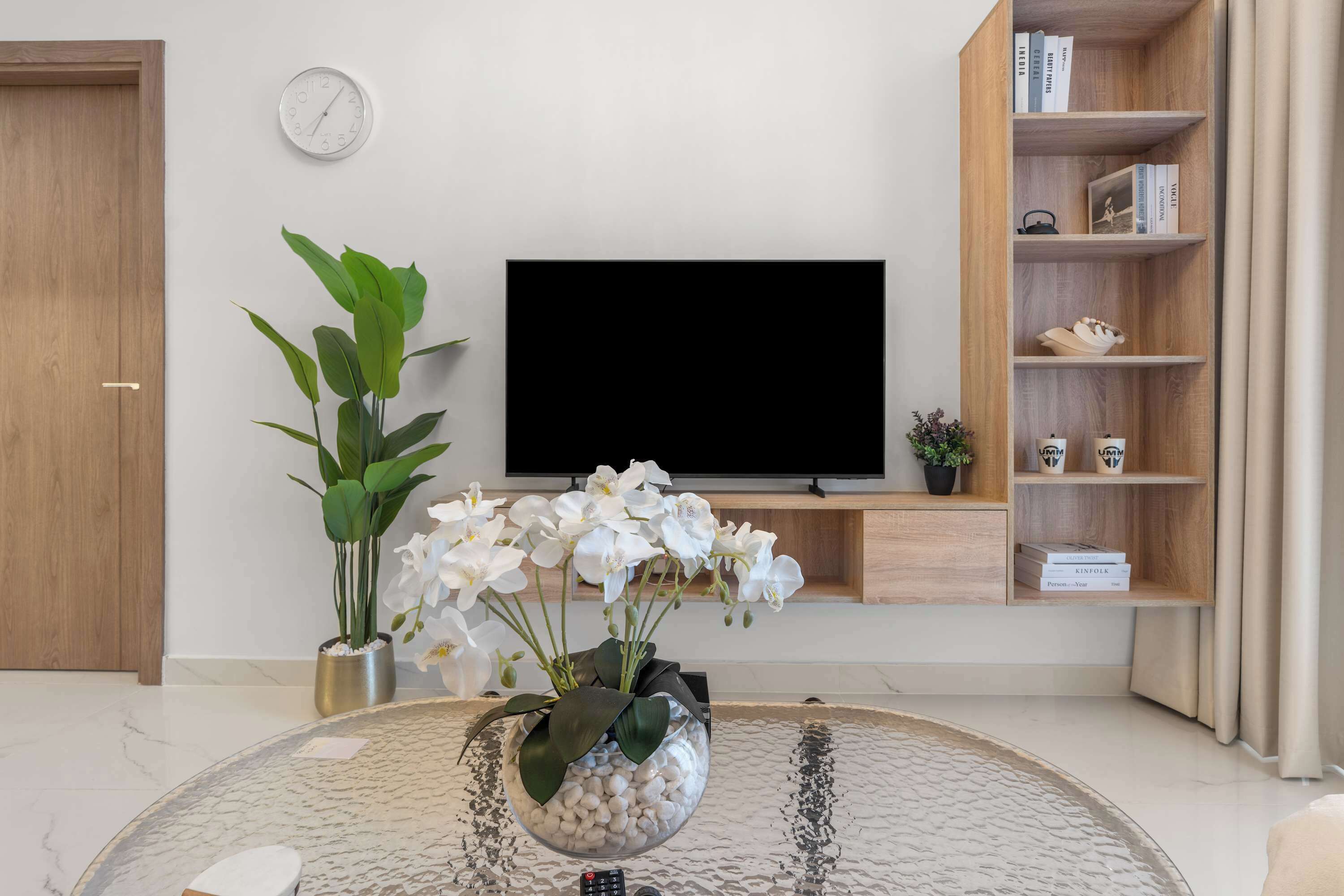 Una sala de estar con televisor de pantalla plana, una estantería, una planta en maceta y una mesa de centro.