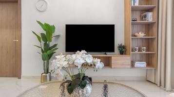 Una sala de estar con televisor de pantalla plana, una estantería, una planta en maceta y una mesa de centro.