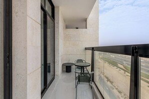 Ein Balkon mit Glastür, einem kleinen runden Tisch und einem Stuhl, mit Blick auf eine Autobahn.