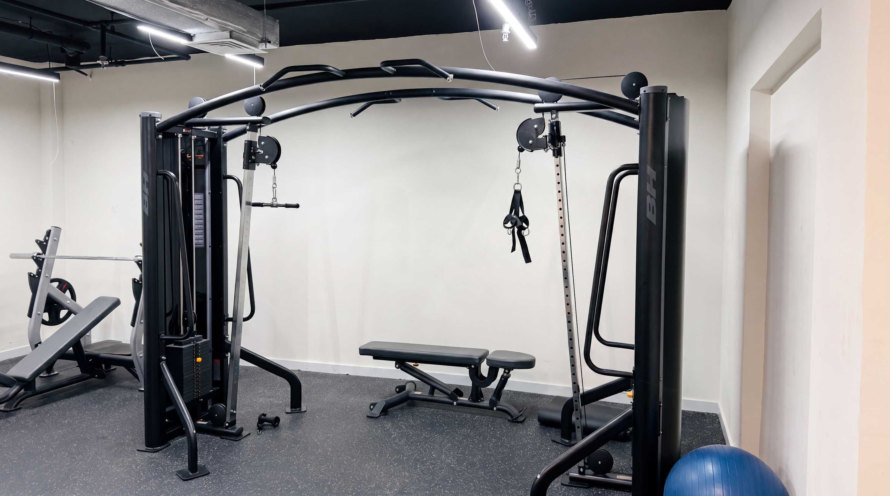 Un gimnasio con equipo de levantamiento de pesas, una banca y pelotas de ejercicio.