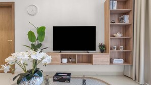 Moderni olohuone, jossa on litteänäyttöinen televisio, kirjahylly, kello ja koriste-esineillä varustettu sohvapöytä.