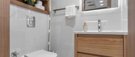 A modern bathroom with a toilet, shower, vanity, and a mirror.