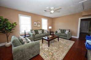 A living room with two green sofas, a coffee table, and a patterned rug. - Cotton Cottage - Cozy Galveston Getaway (Galveston)