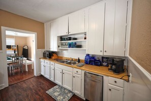 A compact kitchen with white cabinets, a wooden countertop, and a built-in dishwasher. - Cotton Cottage - Cozy Galveston Getaway (Galveston)