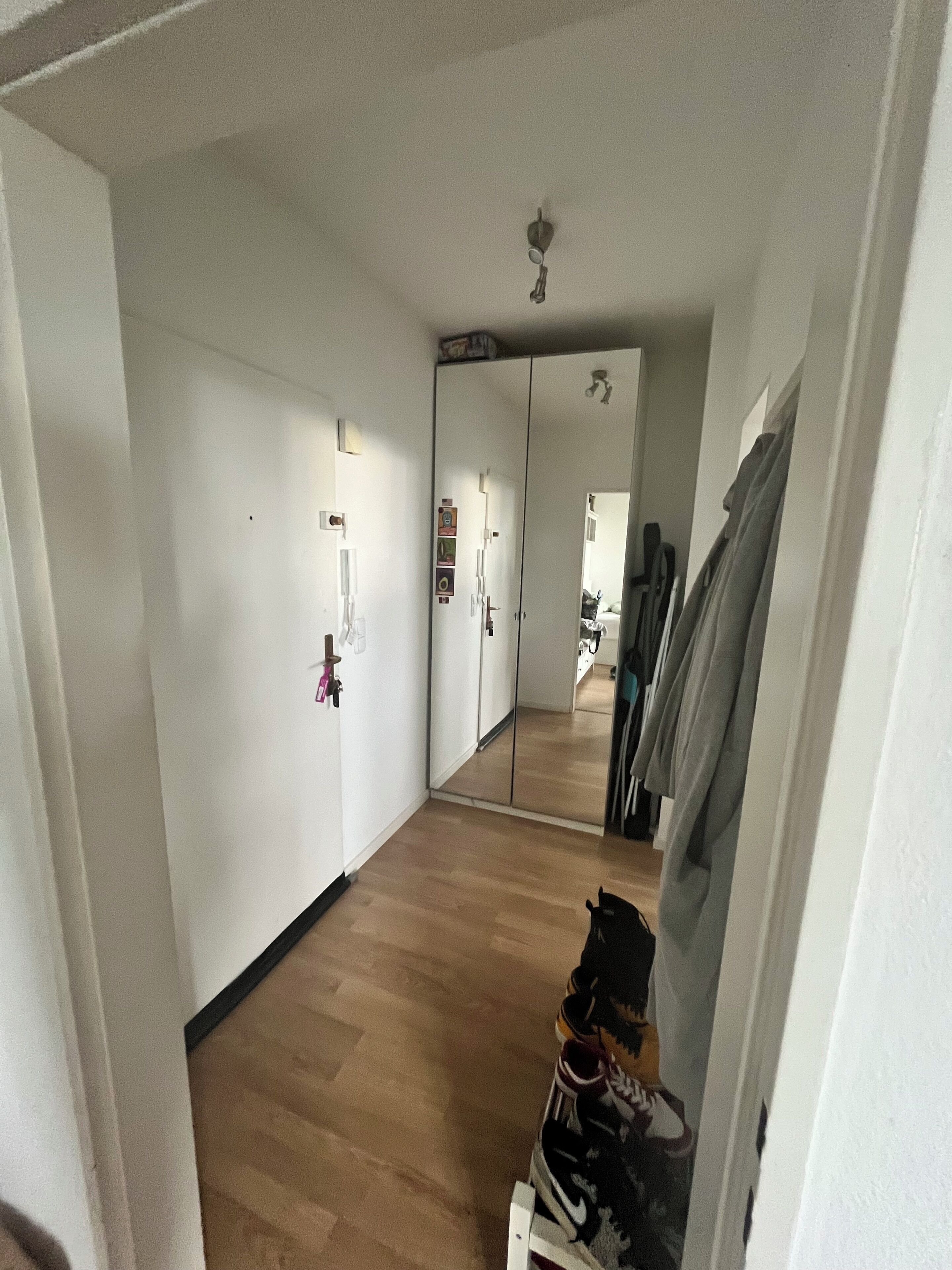 Ein Flur mit Holzboden, einem Spiegel und einem Kleiderschrank mit hängender Kleidung.