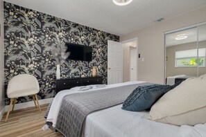 A bedroom with a bed, a dresser, a chair, and a wall-mounted TV.