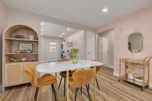 A dining area with a marble table, two chairs, a vase with flowers, and a gold cart with glassware.