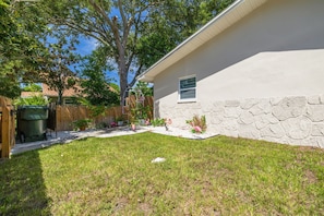 Patio trasero residencial con césped, un muro de piedra y una valla de madera.