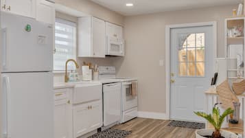 A kitchen with white cabinetry, a microwave, a dishwasher, and a stove. There is a door with a window, a plant, and a countertop with kitchen utensils.