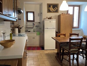 A kitchen with a white refrigerator, wooden cabinets, a dining table with chairs, and a window with natural light. - Relaxation and culture, blending history and nature in Umbria’s most beautiful spots. (Acera)