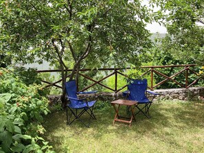 An outdoor seating area with two blue folding chairs and a small wooden table, surrounded by lush greenery and a stone wall. - Relaxation and culture, blending history and nature in Umbria’s most beautiful spots. (Acera)